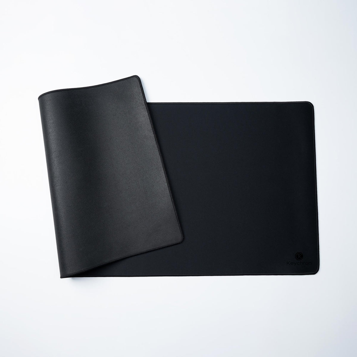 Keychron Desk Mat in Black, partly unrolled to show the rubber base